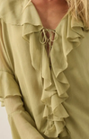 Close-up of a woman wearing a pale sage green blouse with layered ruffles and a tie-front neckline.