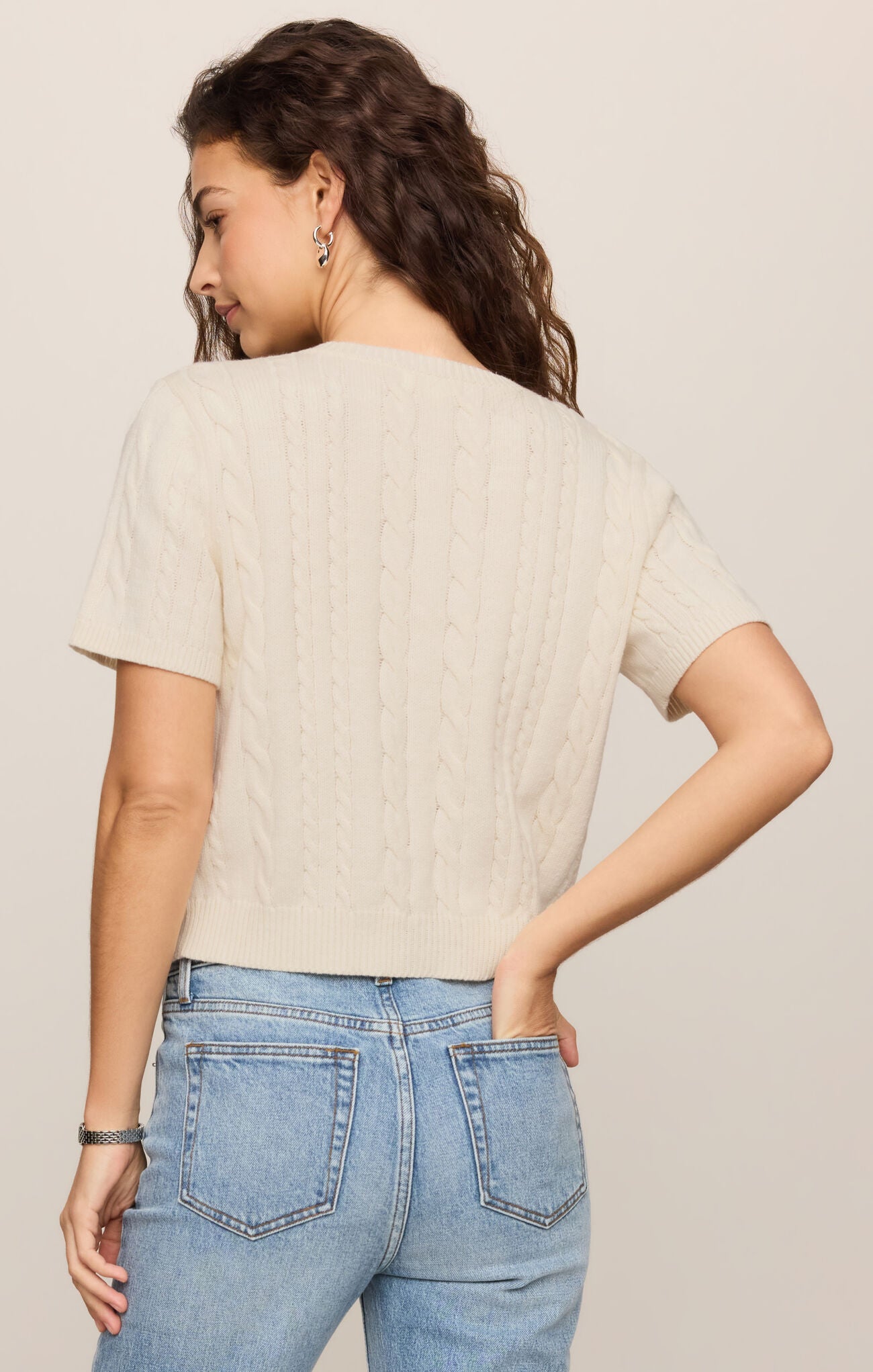 Woman wearing a beige sweater and blue jeans against a plain background
