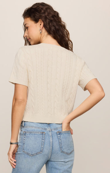 Woman wearing a beige sweater and blue jeans against a plain background
