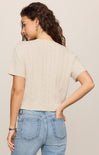 Woman wearing a beige sweater and blue jeans against a plain background