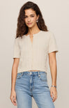 Woman wearing a beige top and blue jeans against a plain background