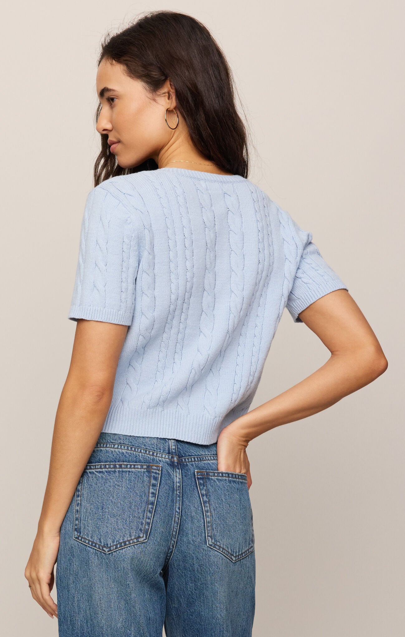 Woman wearing a light blue textured top and blue jeans against a beige background