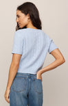 Woman wearing a light blue textured top and blue jeans against a beige background