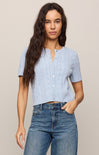 Woman wearing a light blue textured shirt and blue jeans against a beige background