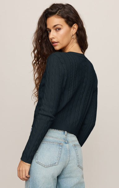 Woman wearing a black long-sleeve top and light blue jeans against a beige background