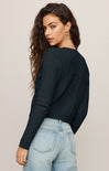 Woman wearing a black long-sleeve top and light blue jeans against a beige background