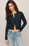 Woman wearing a dark blue cardigan over a black top with light blue jeans on a beige background