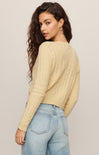 Woman wearing a beige sweater and light blue jeans against a plain background