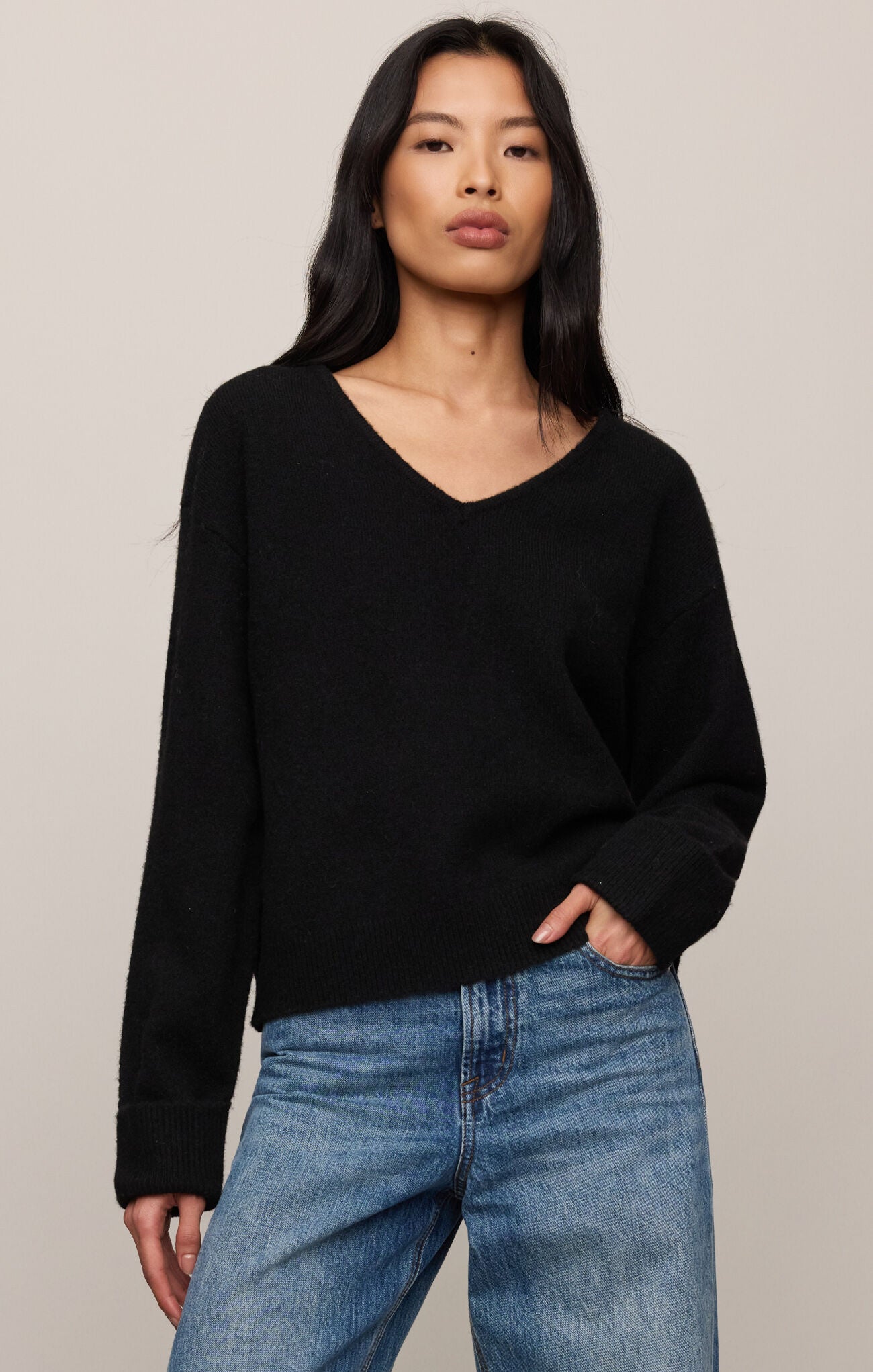 Woman wearing a black sweater and blue jeans against a plain background