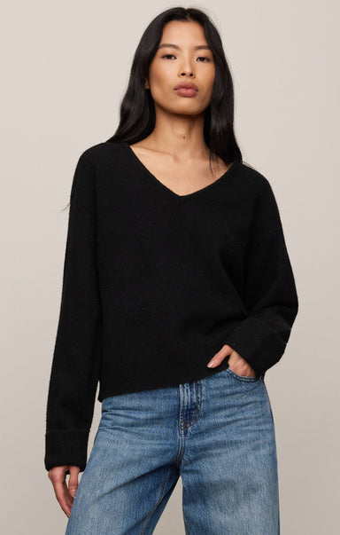 Woman wearing a black sweater and blue jeans against a plain background
