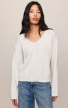 Woman wearing a white sweater and blue jeans against a beige background