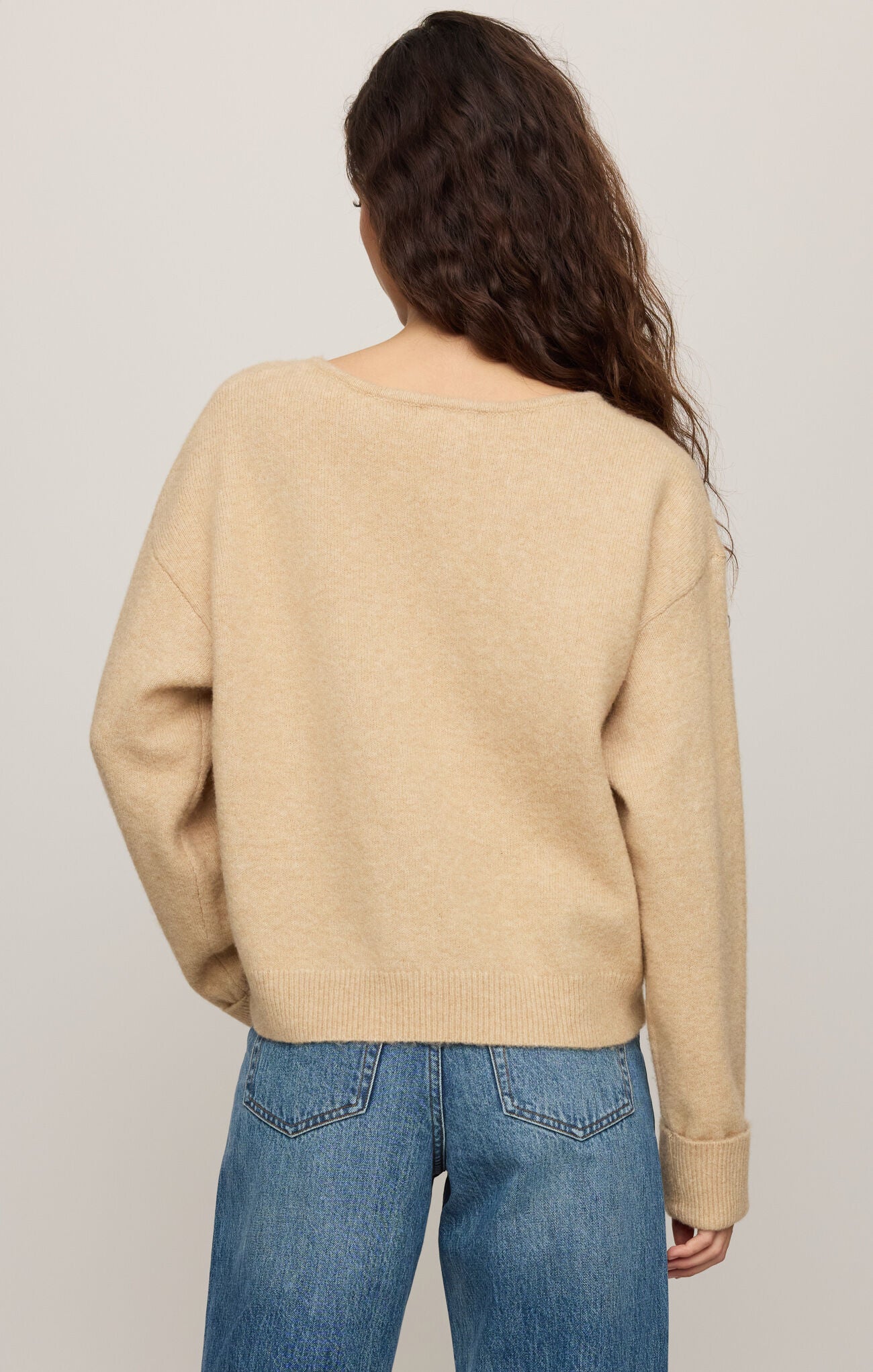 Person wearing a beige sweater and blue jeans on a plain background