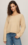 Woman wearing a beige sweater and blue jeans against a plain background