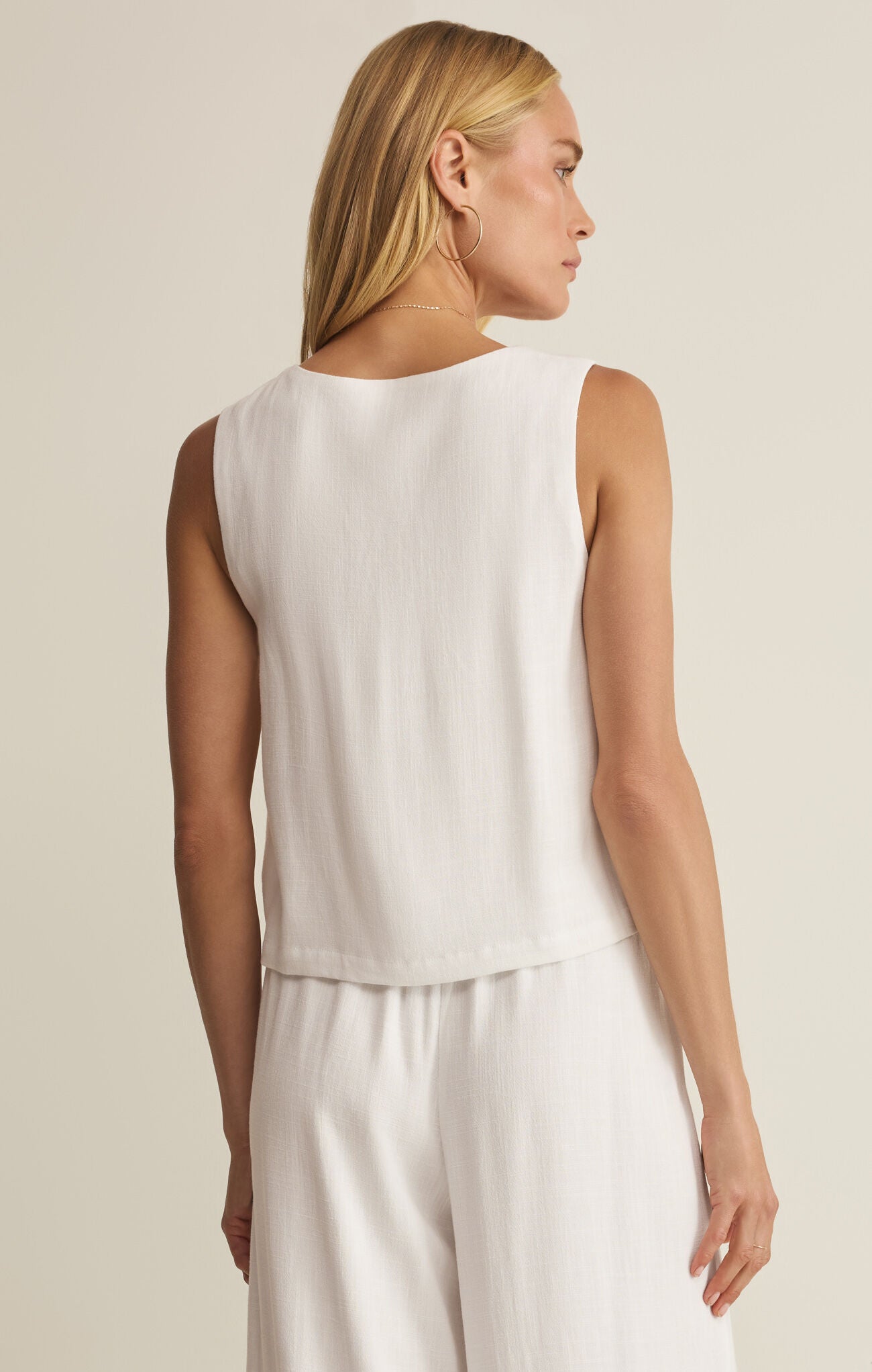 Woman wearing a white sleeveless top and pants against a beige background