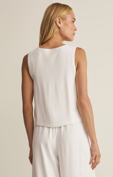 Woman wearing a white sleeveless top and pants against a beige background