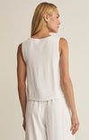 Woman wearing a white sleeveless top and pants against a beige background