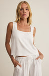 Woman wearing a white sleeveless top and pants against a beige background