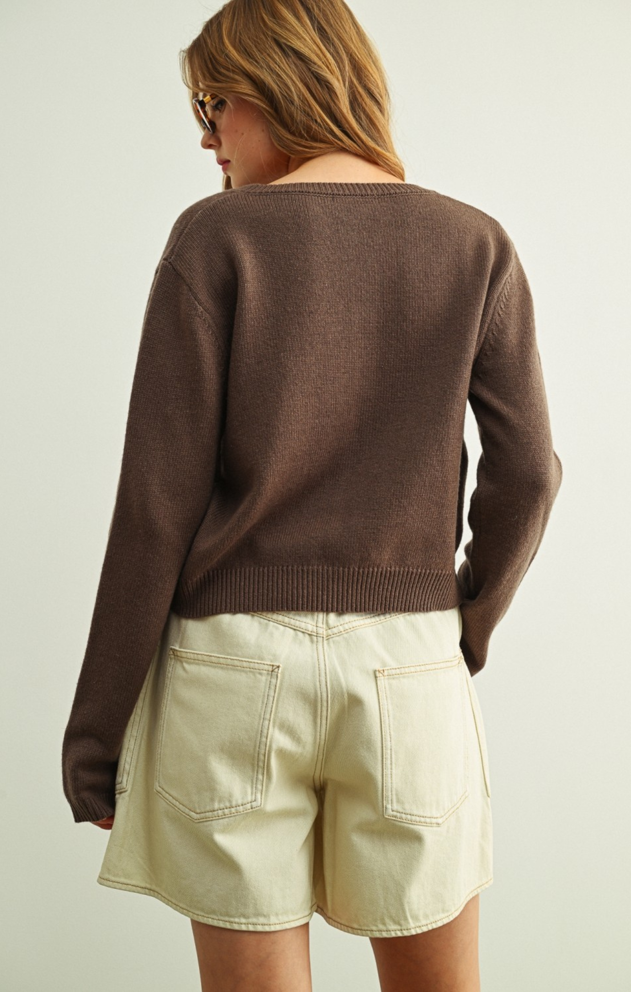 Person wearing a brown sweater and beige shorts on a plain background