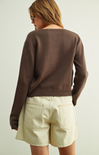Person wearing a brown sweater and beige shorts on a plain background