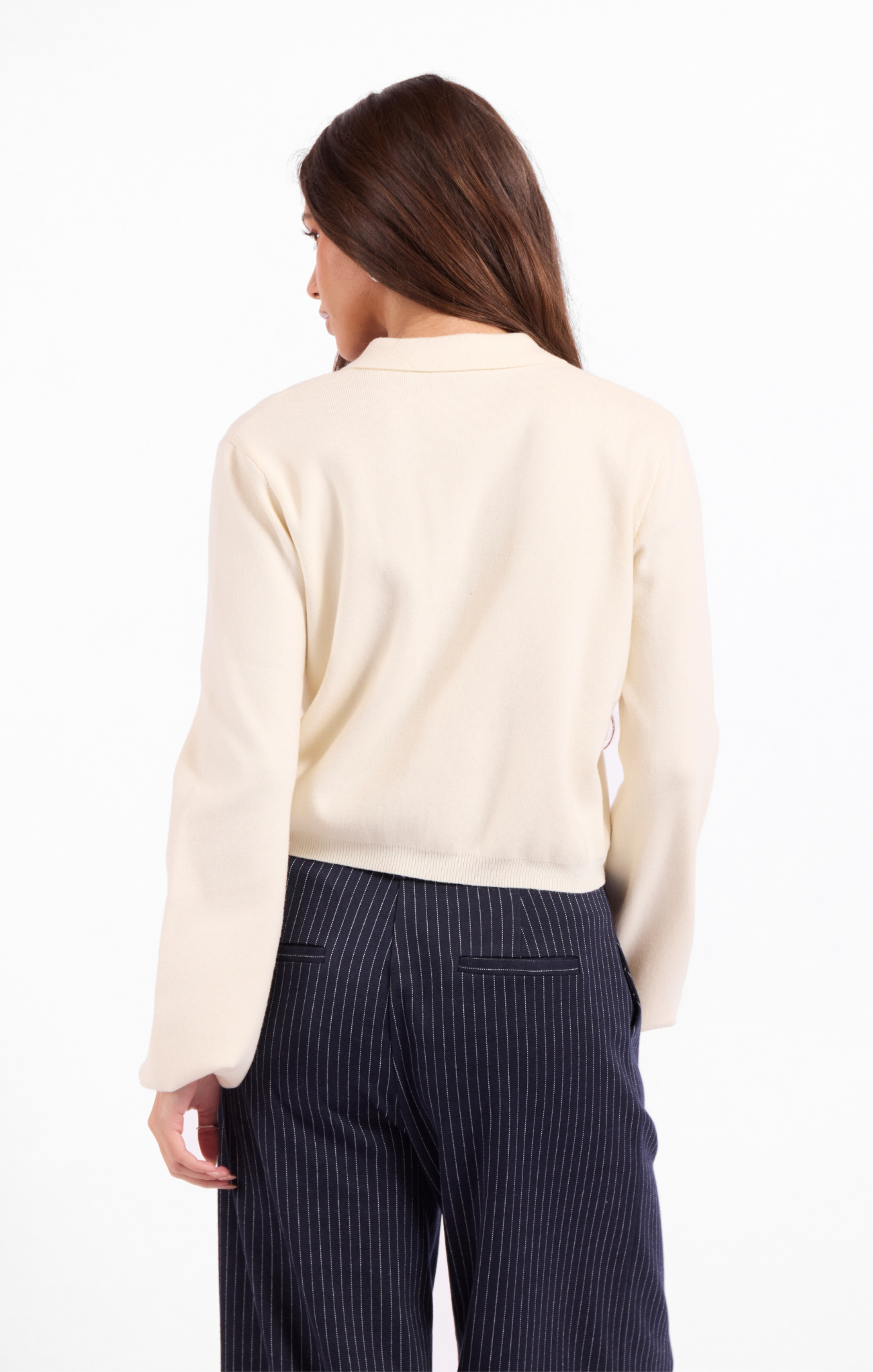 Woman wearing a cream sweater and dark pinstripe pants on a white background