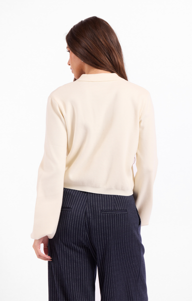 Woman wearing a cream sweater and dark pinstripe pants on a white background