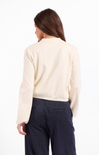 Woman wearing a cream sweater and dark pinstripe pants on a white background