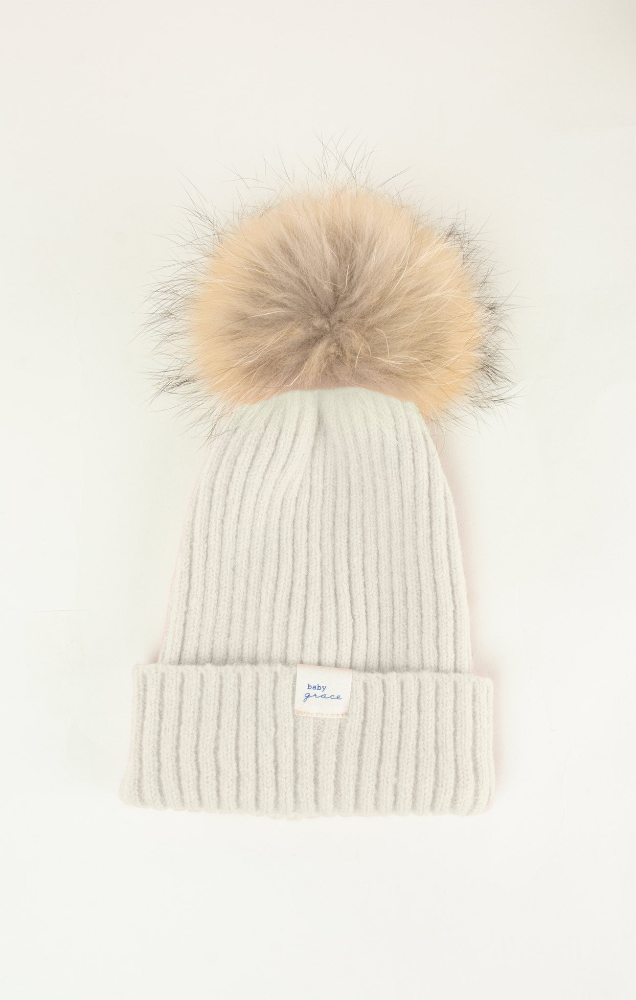 White knit beanie with a large beige fur pom-pom on a white background
