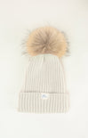 White knit beanie with a large beige fur pom-pom on a white background