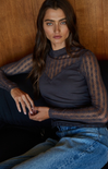 Woman wearing a dark blue lace top and jeans against a wooden background