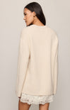 Woman wearing a beige sweater over a lace dress on a plain background
