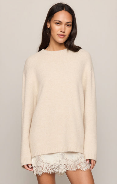 Woman wearing a beige sweater over a lace dress on a plain background