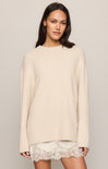Woman wearing a beige sweater over a lace dress on a plain background