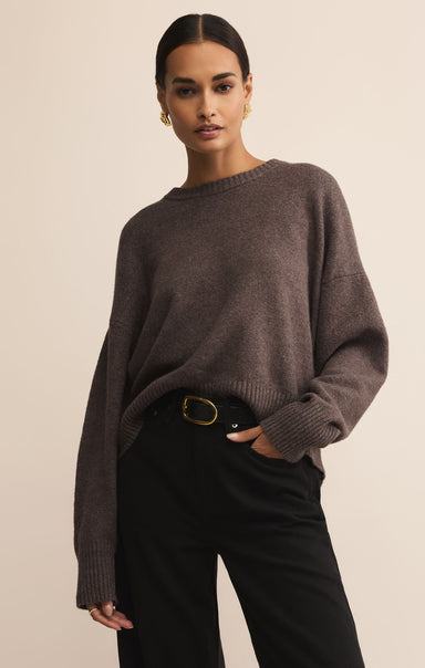 Woman wearing a brown sweater and black pants against a beige background
