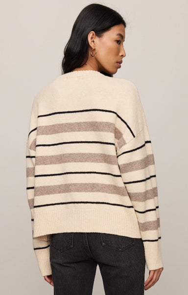 Woman wearing a cream sweater with black and brown horizontal stripes on a plain background