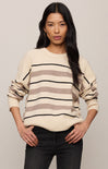 Woman wearing a cream sweater with brown and black stripes against a plain background
