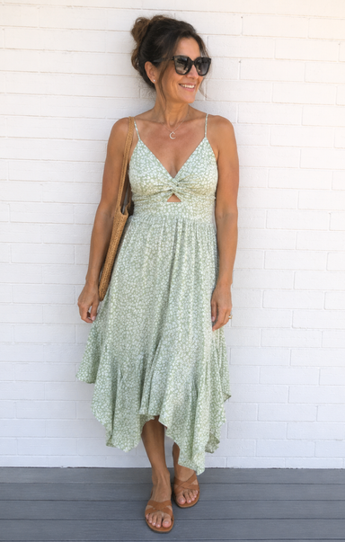 Woman wearing a light green floral dress against a white brick wall.