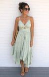 Woman wearing a light green floral dress against a white brick wall.