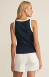 Woman wearing a navy sleeveless top with lace trim and white shorts on a beige background