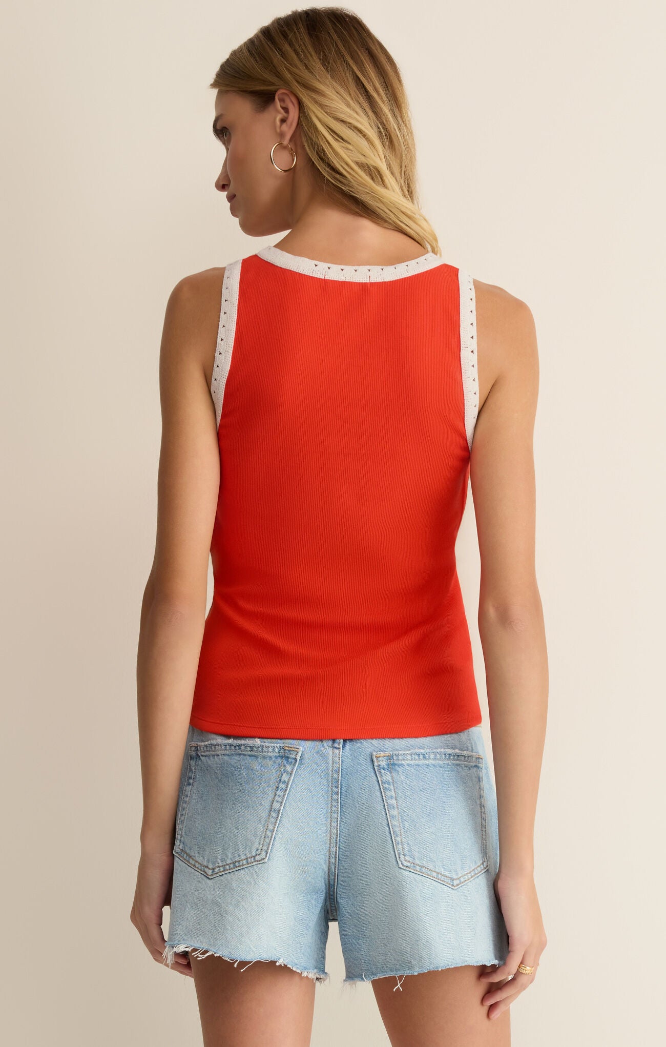 Woman wearing a red tank top with lace trim and denim shorts on a beige background