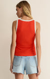 Woman wearing a red tank top with lace trim and denim shorts on a beige background