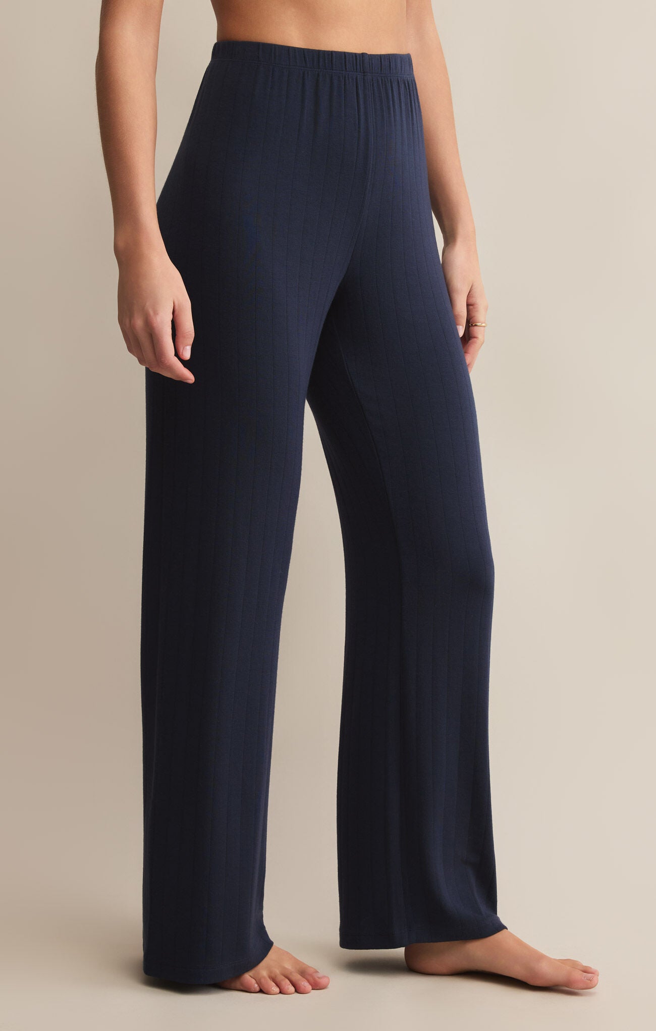 A person standing and wearing navy high-waisted, full-length ribbed pants made of modal and spandex.