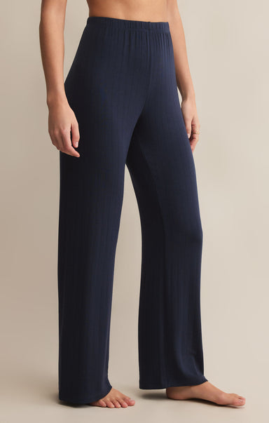 A person standing and wearing navy high-waisted, full-length ribbed pants made of modal and spandex.