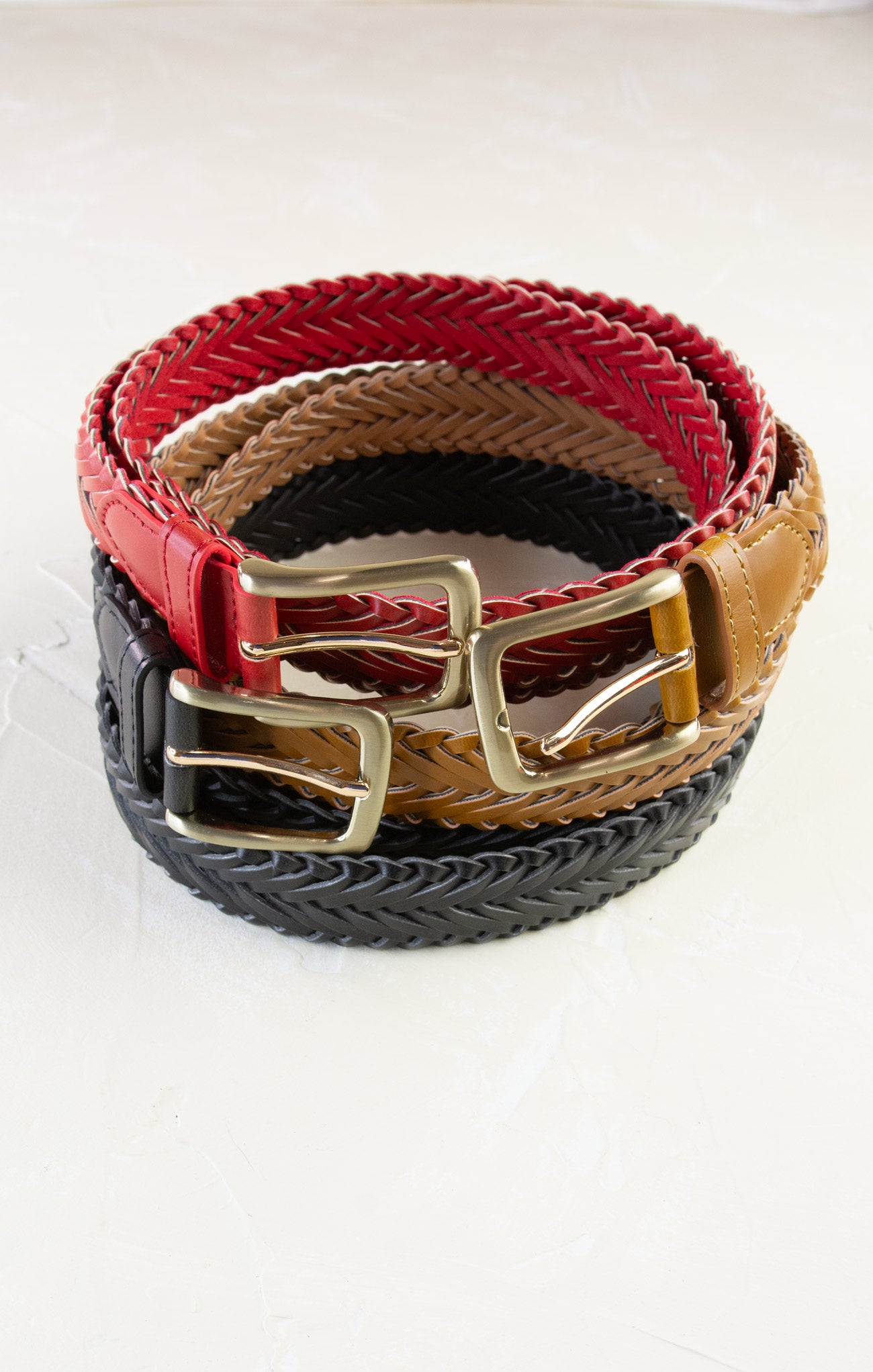 Three braided belts in red, brown, and black with gold buckles on a white background.