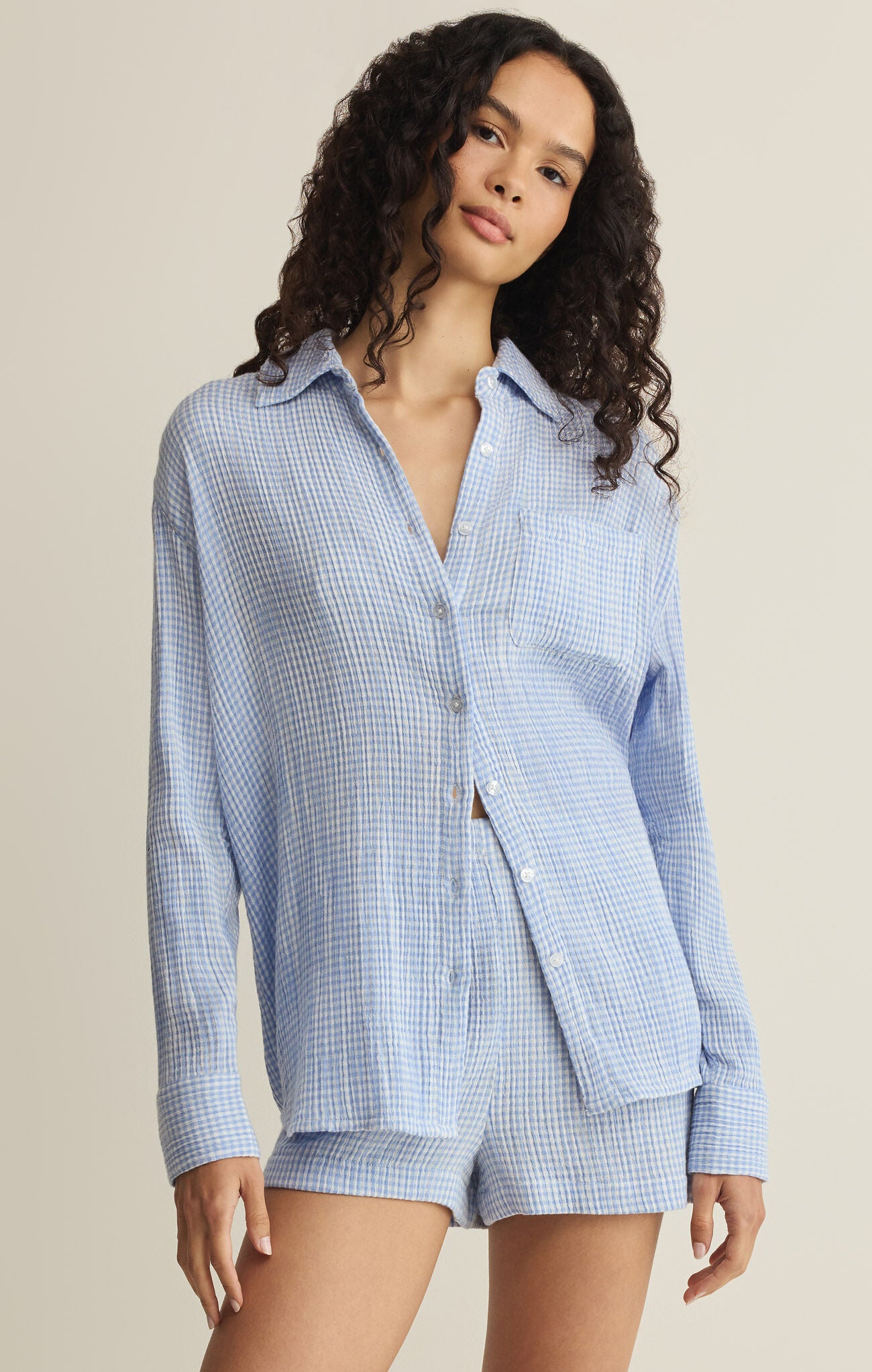 Woman wearing a blue checkered shirt and shorts set against a beige background