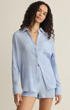 Woman wearing a blue checkered shirt and shorts set against a beige background