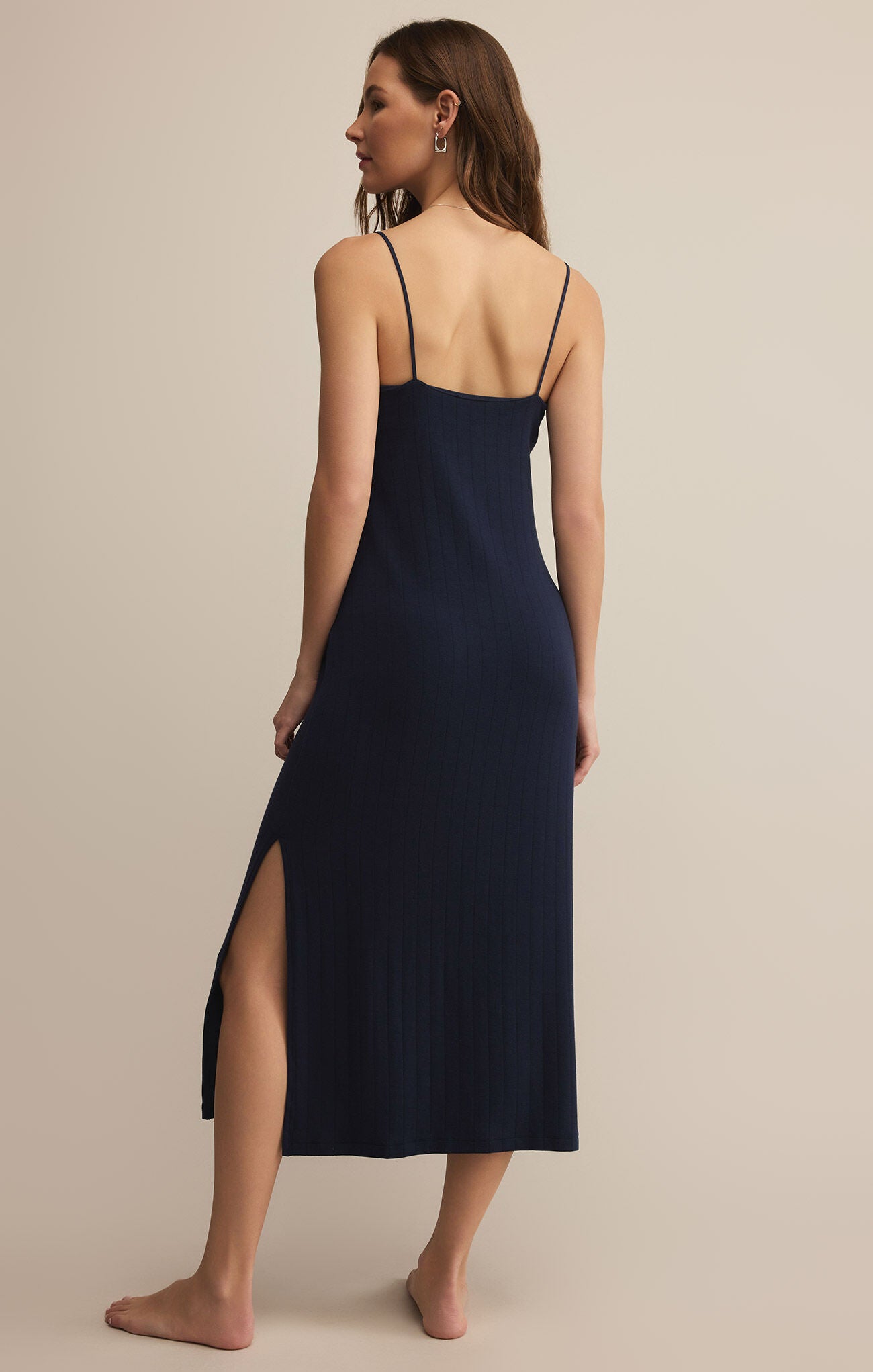 A woman wearing a navy, sleeveless, midi-length dress with a scoop neckline and spaghetti straps. The dress appears to be made of a lightweight, soft fabric and has a regular fit.