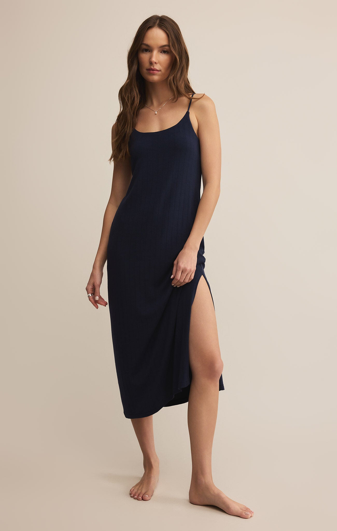 A woman wearing a navy, sleeveless, midi-length dress with a scoop neckline and spaghetti straps. The dress appears to be made of a lightweight, soft fabric and has a regular fit.