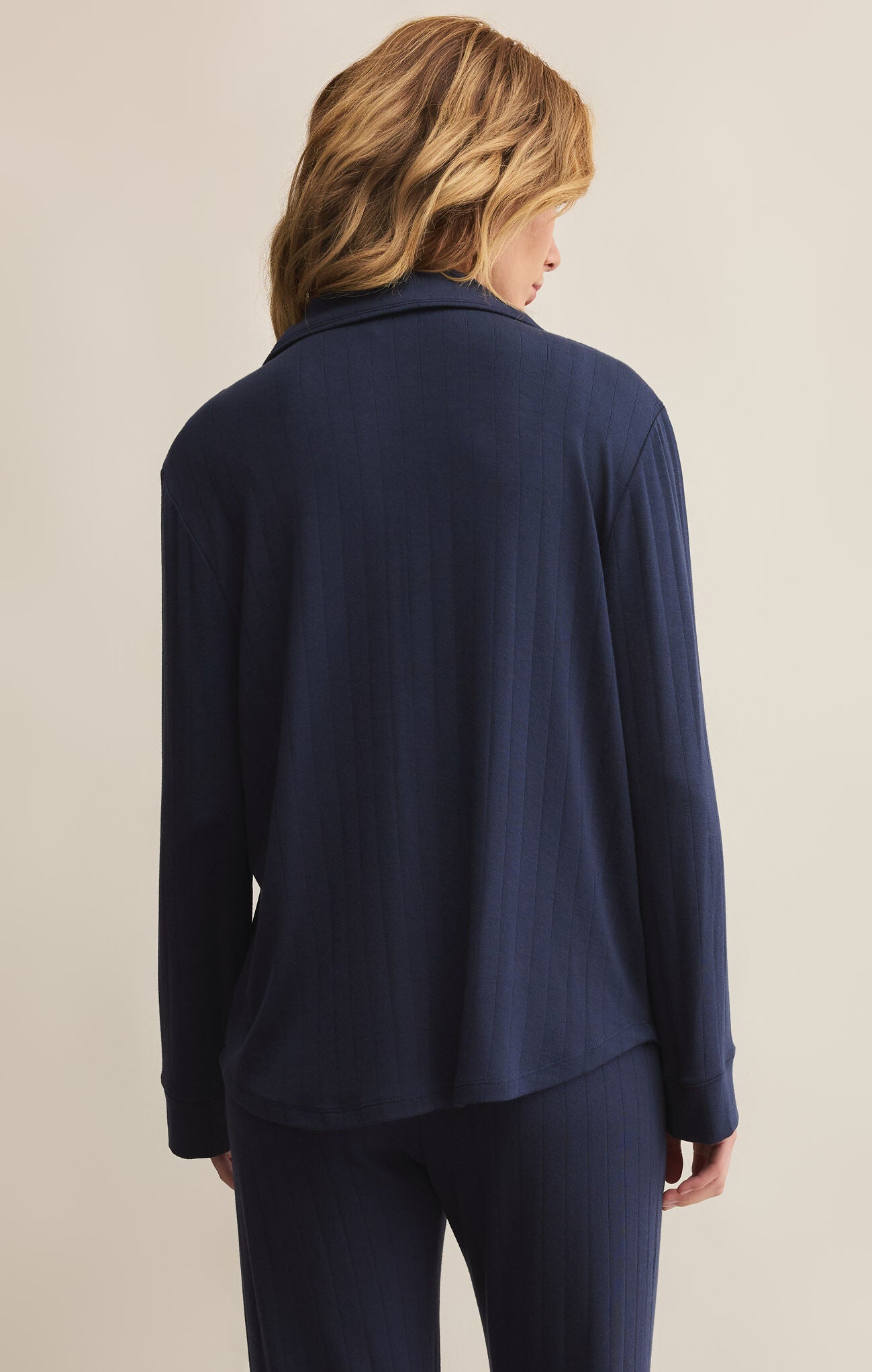 A woman wearing a navy blue, collared, long-sleeved button-front rib top with a relaxed fit.
