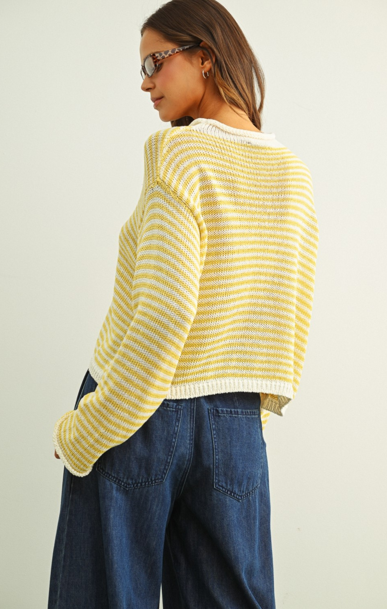 Person wearing a yellow striped sweater and blue jeans against a plain background