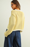 Person wearing a yellow striped sweater and blue jeans against a plain background